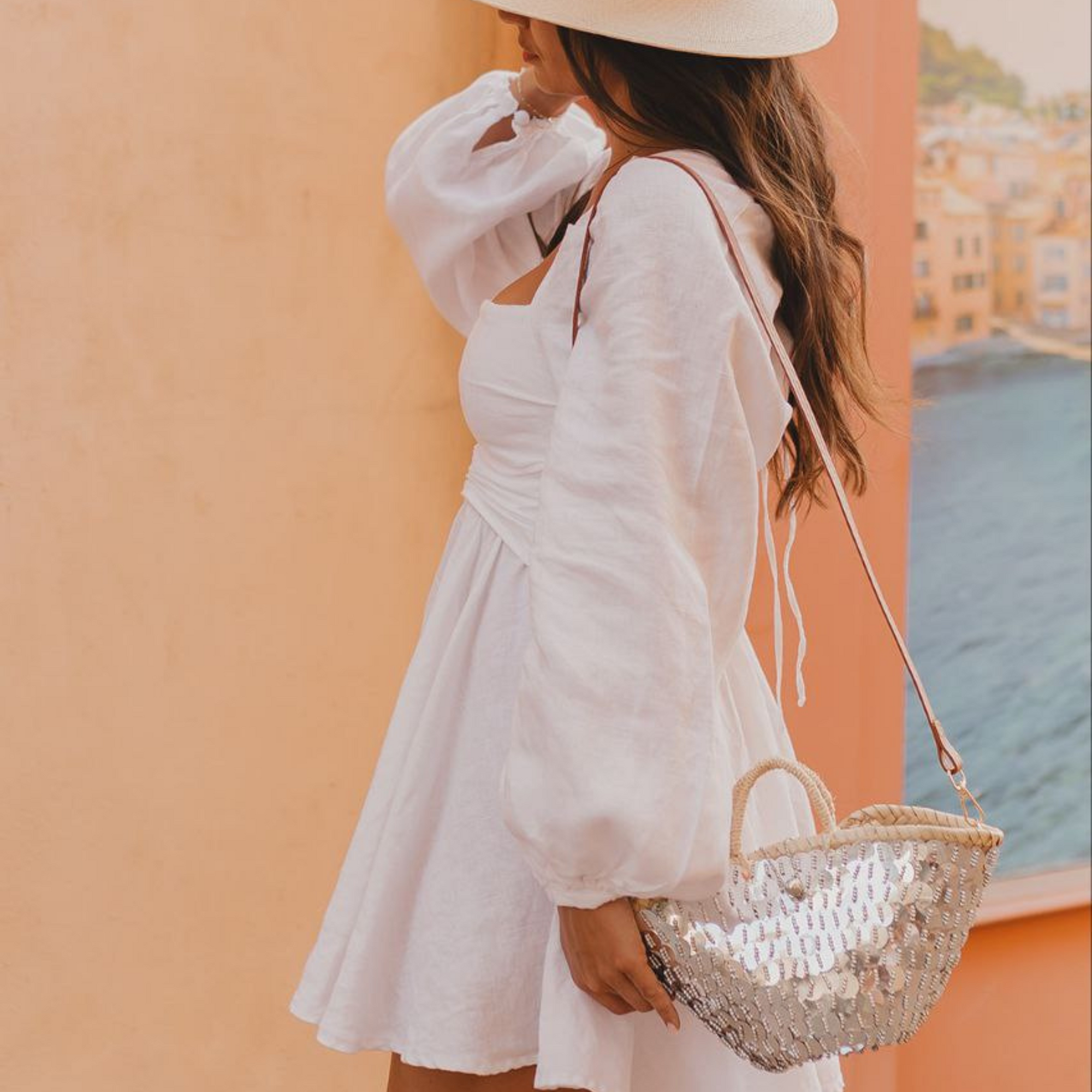Woman wearing handmade mirror crossbody bag with braided top handles and leather strap, styled with white dress