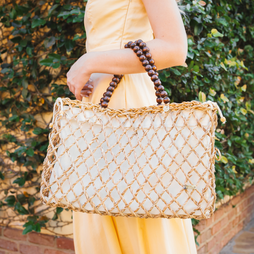 Woman in a yellow dress carrying a medium woven tote bag with wooden bead handles