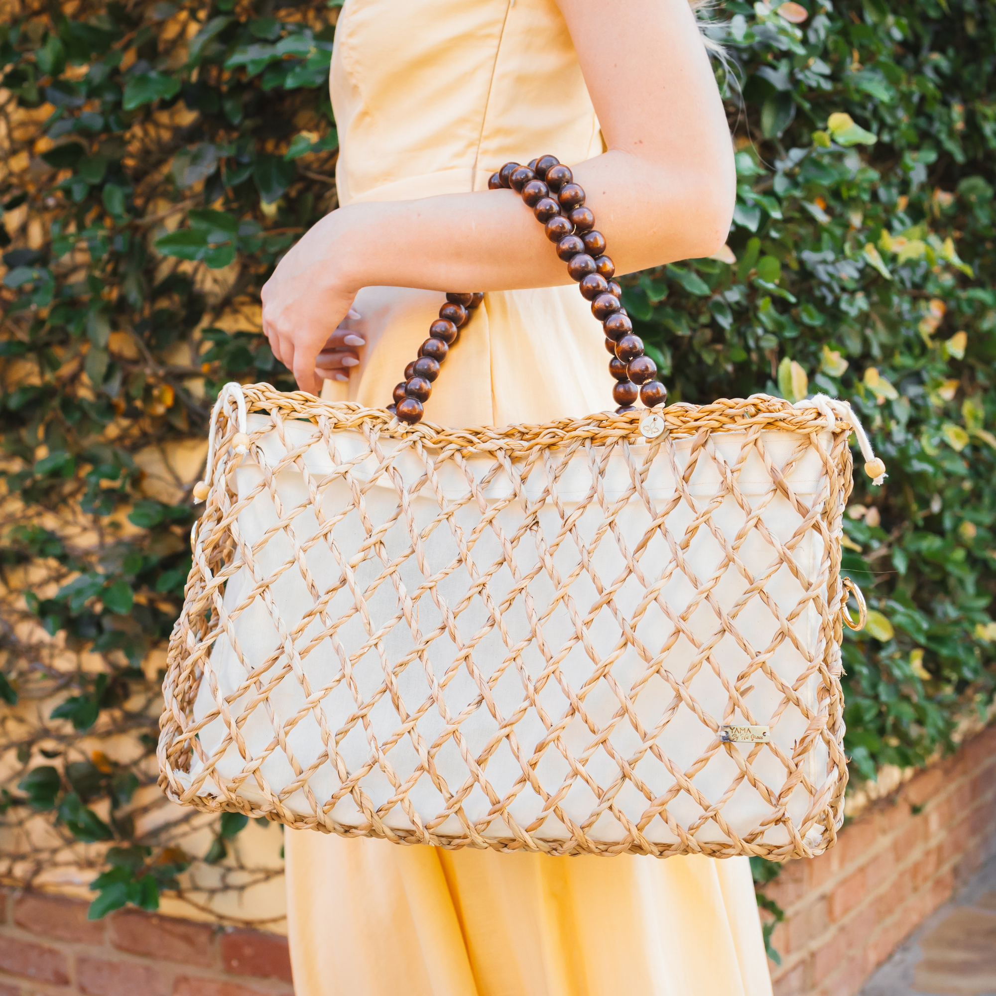 Woman in a yellow dress carrying a medium woven tote bag with wooden bead handles