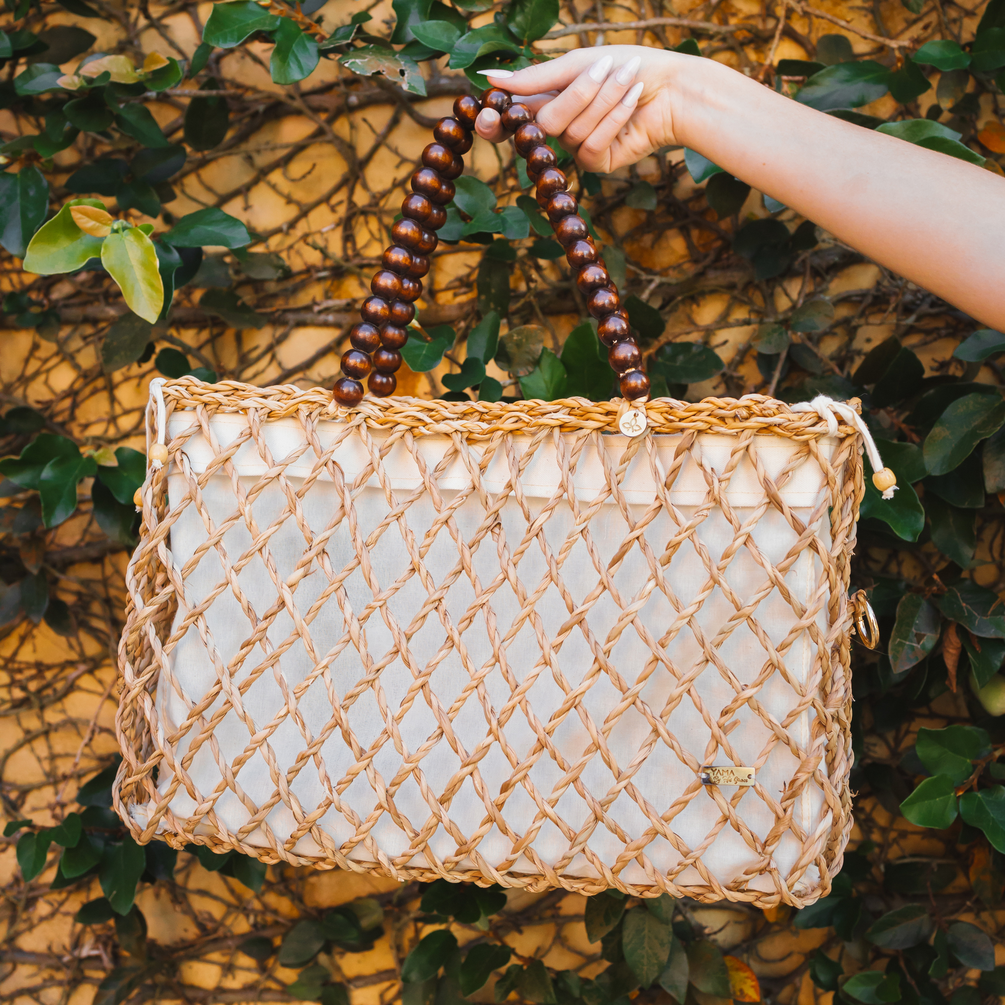 Hand holding the woven tote bag in front of leafy wall background