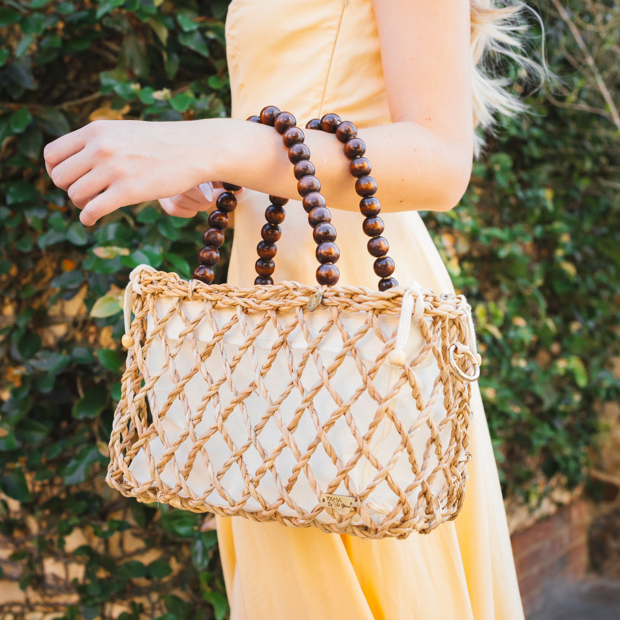 Woman in yellow dress holding the small version of the woven tote bag by her arm