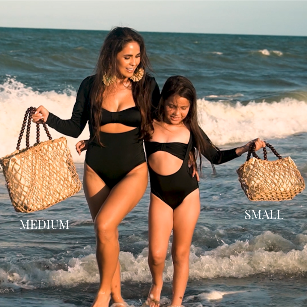 Mother and daughter walking by the ocean holding medium and small sizes of the woven tote bag