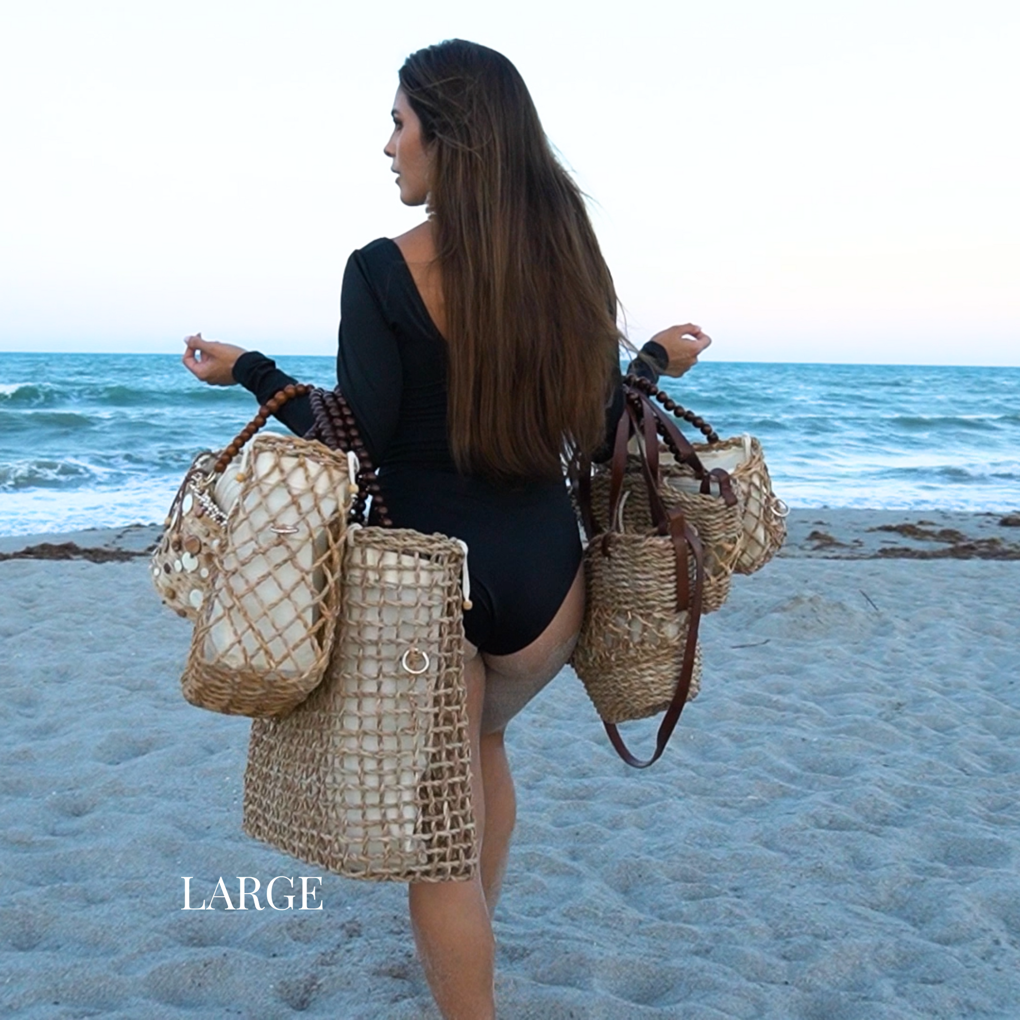 Woman walking on the beach carrying large woven tote bags in both hands
