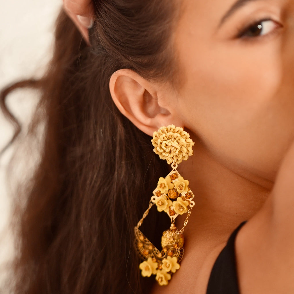 Close-up of a woman wearing gold floral earrings with a neutral background