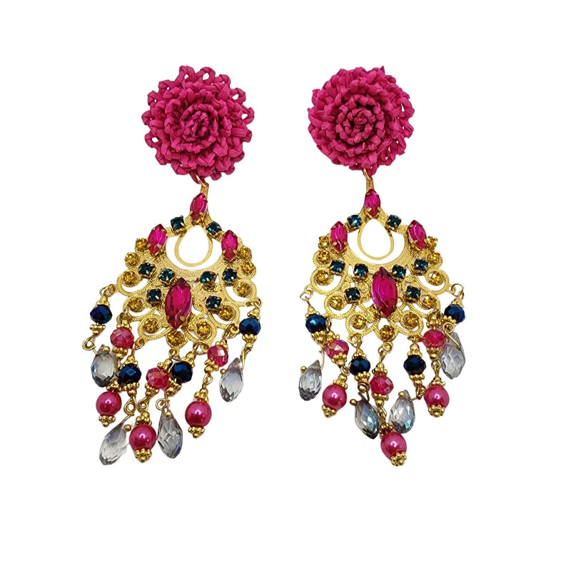 These handcrafted earrings are shaped like flowers made from banana fiber painted in pink, adorned with pink, blue, and clear gemstones cascading down a golden sheet. 