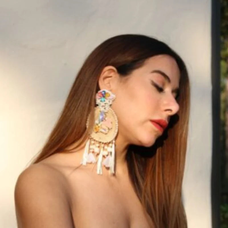 This majestic sun-shaped earring is crafted from natural fibers, embroidered with small Murano beads, and combined with fine jewelry. It is further adorned with Murano stones, dangling tassels, puffy beads, and delicate feathers, showcasing a radiant design. Handmade with Banana Tree Fibers.