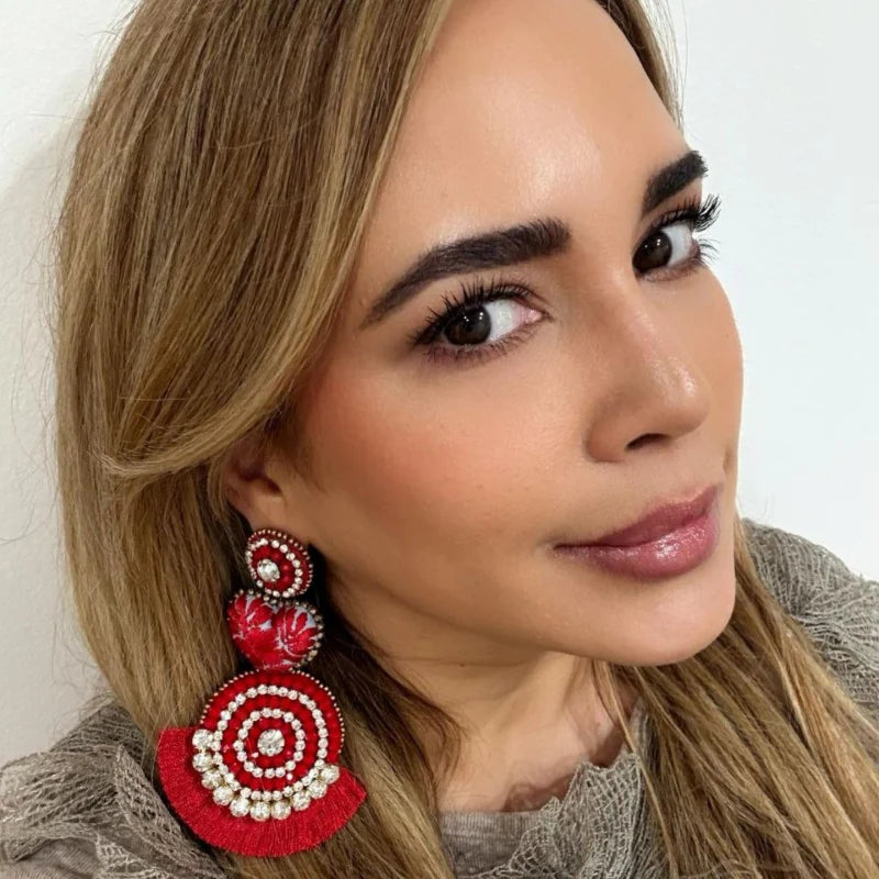 These vibrant earrings blend red beads and sparkling crystals in a charming circular design. Featuring bright gemstones, textured floral shapes