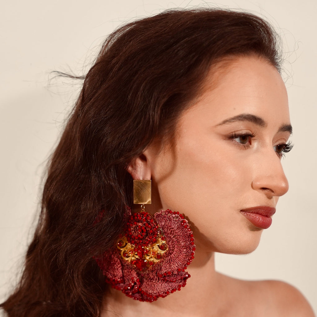 Woman wearing red earrings with gold accents against a neutral background
