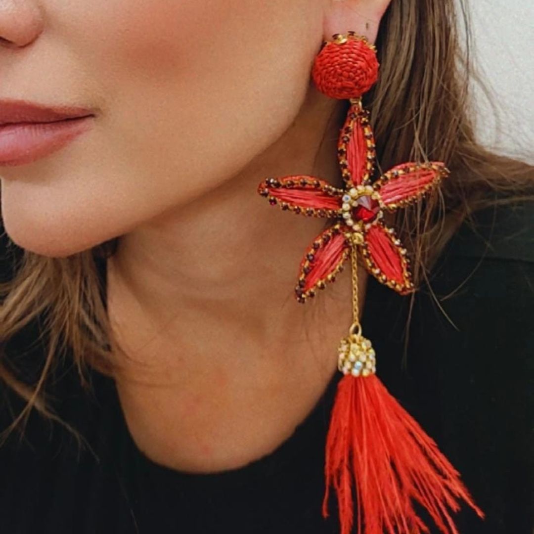 Close-up of a woman wearing a red flower-shaped earring with a gold center and long red feather tassel.