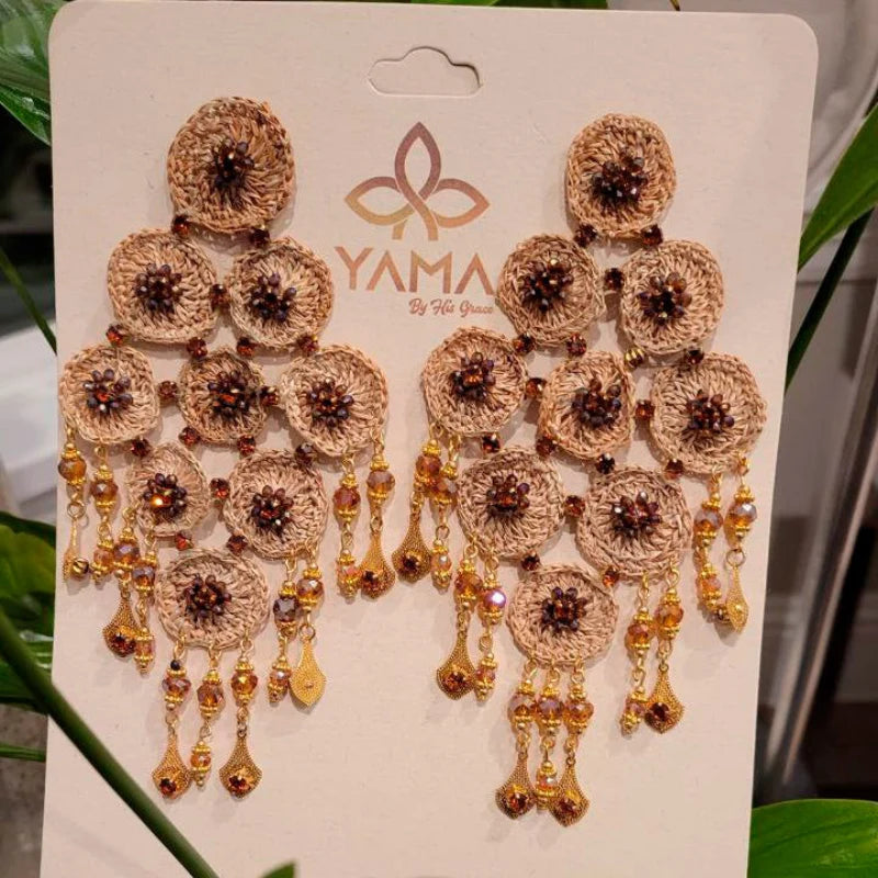 These majestic earrings are shaped like a large rhombus, symbolizing a mountain. Adorned with gemstones and dangling Murano stones at the edges, they feature fine jewelry at the base, creating a shimmering appearance. Handmade entirely with Banana Tree Fibers, these earrings reflect God’s wonder and the natural beauty of craftsmanship.