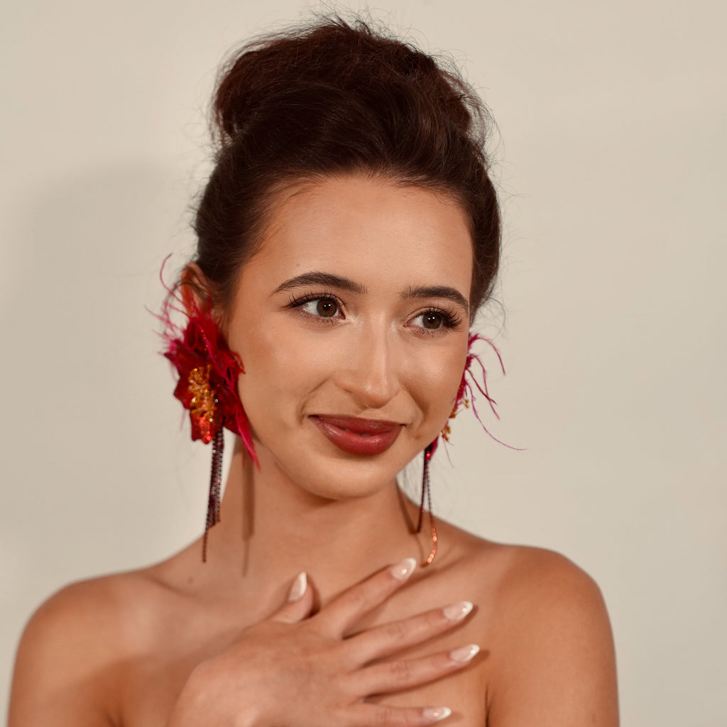Woman with floral earrings and a black top against a plain background