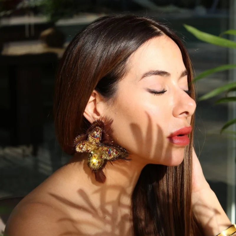 These gorgeous earrings feature a butterfly-like shape, intricately embroidered with small Murano stones, and bordered with colored Murano stones along the edges of the feathers. Symbolizing transformation, like the passage from 1st Corinthians 15:40—"I will transform myself, we could walk on water and fly like butterflies"—these earrings are crafted from Banana Tree Fibers.
