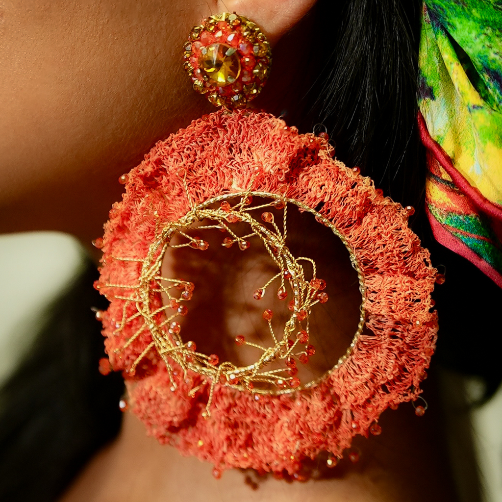 Close-up of a red textured earring with gold accents worn by a person.
