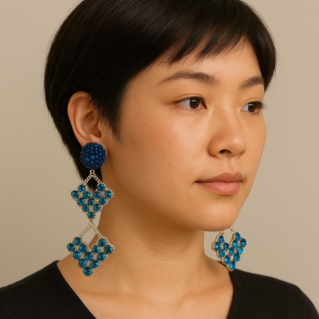 Model wearing large handcrafted silver earrings with blue gemstones and pom-pom accents, styled with a black top