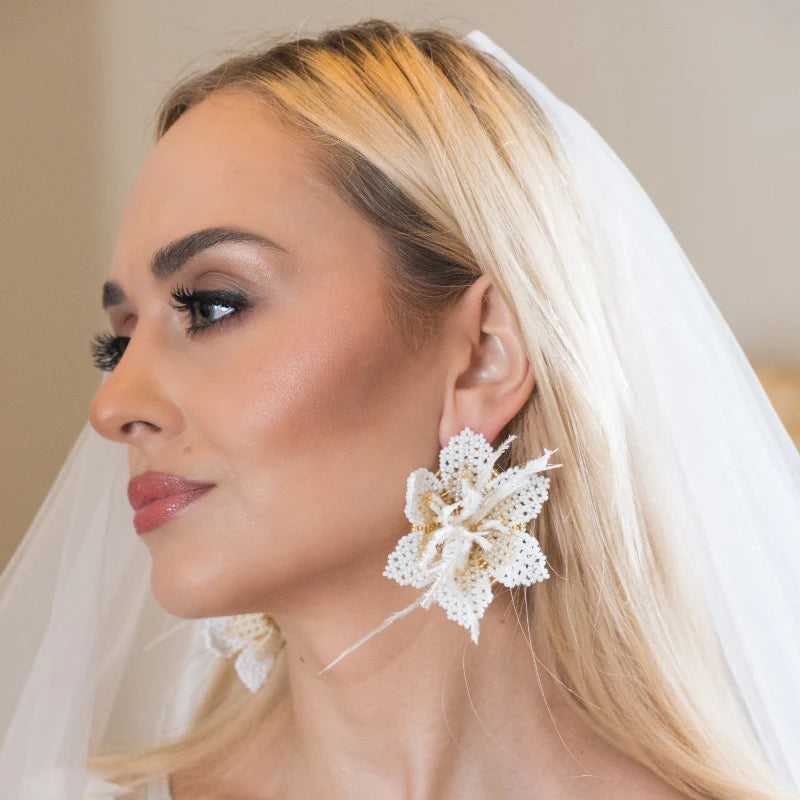 These elegant floral design earrings, crafted with white and gold beads, are adorned with delicate feathers for an ethereal and romantic touch. Perfect for modern, eco-conscious brides, they are a stunning accessory for weddings and special occasions.