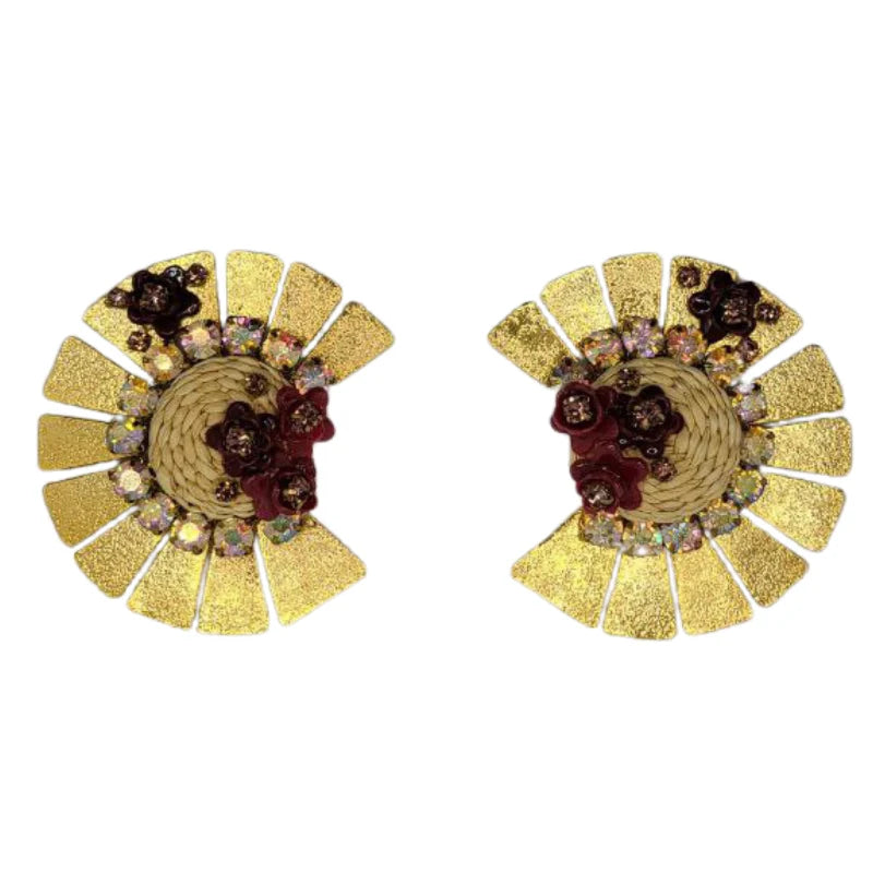 These stunning earrings feature a radiant design with golden fan-shaped panels encircling a woven banana fiber centerpiece. Adorned with delicate burgundy flowers and shimmering crystals, they exude elegance and sophistication.