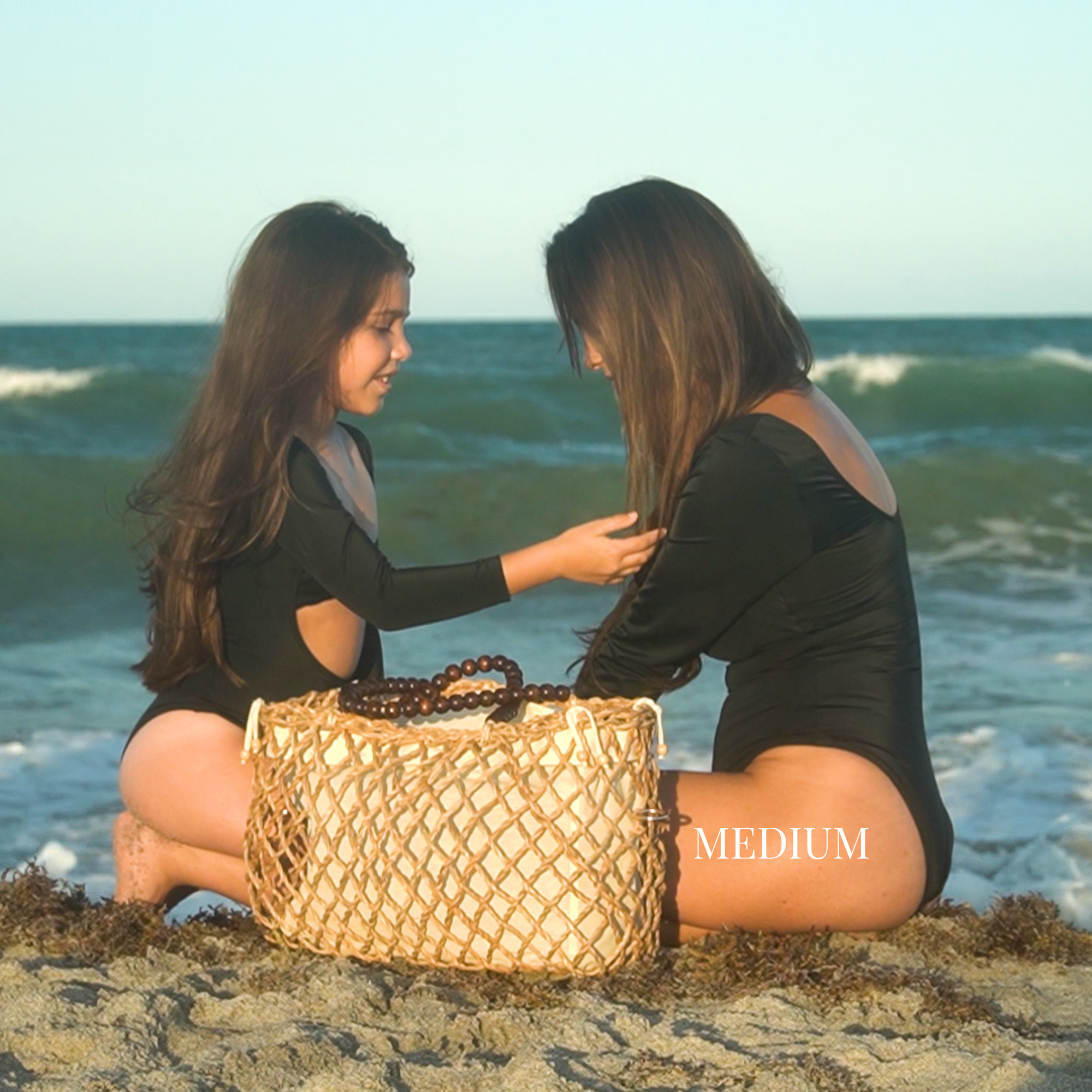 Mother and daughter sitting on the beach with a medium-size woven tote bag between them
