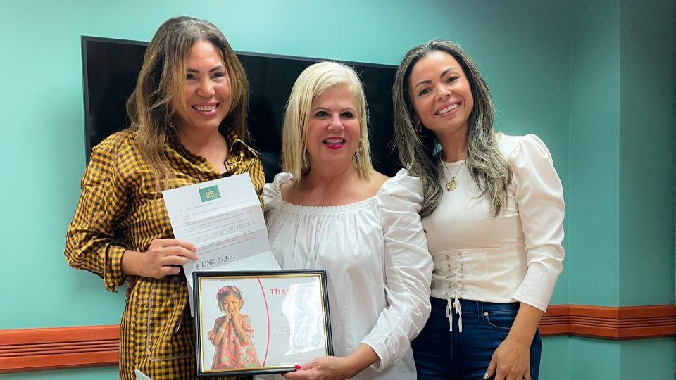 Three women standing in a room with a table, one holding a framed picture.