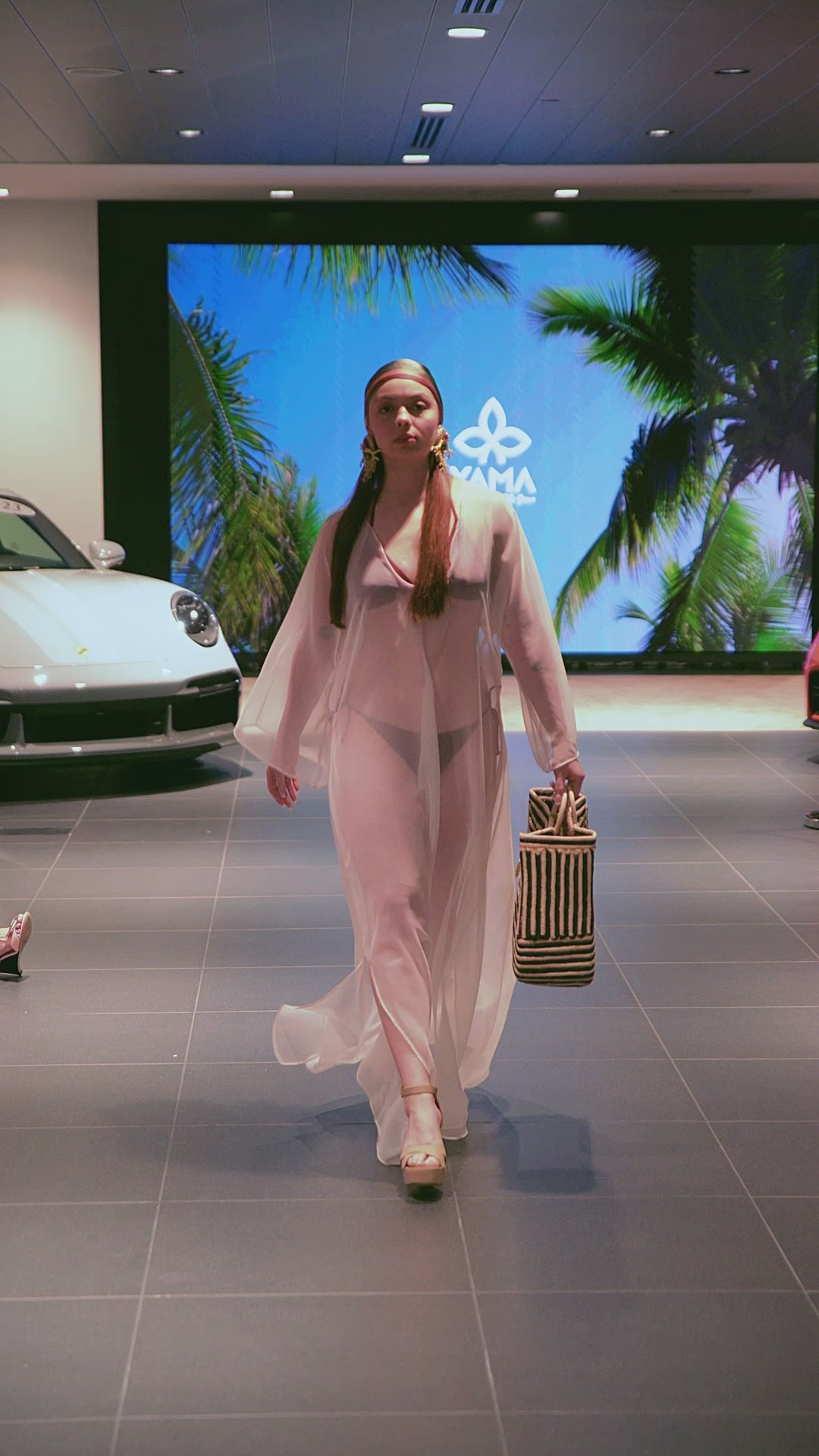 Runway model presenting the Savanna Stripes Beach Tote, highlighting its black-and-beige checkered weave and circular handles
