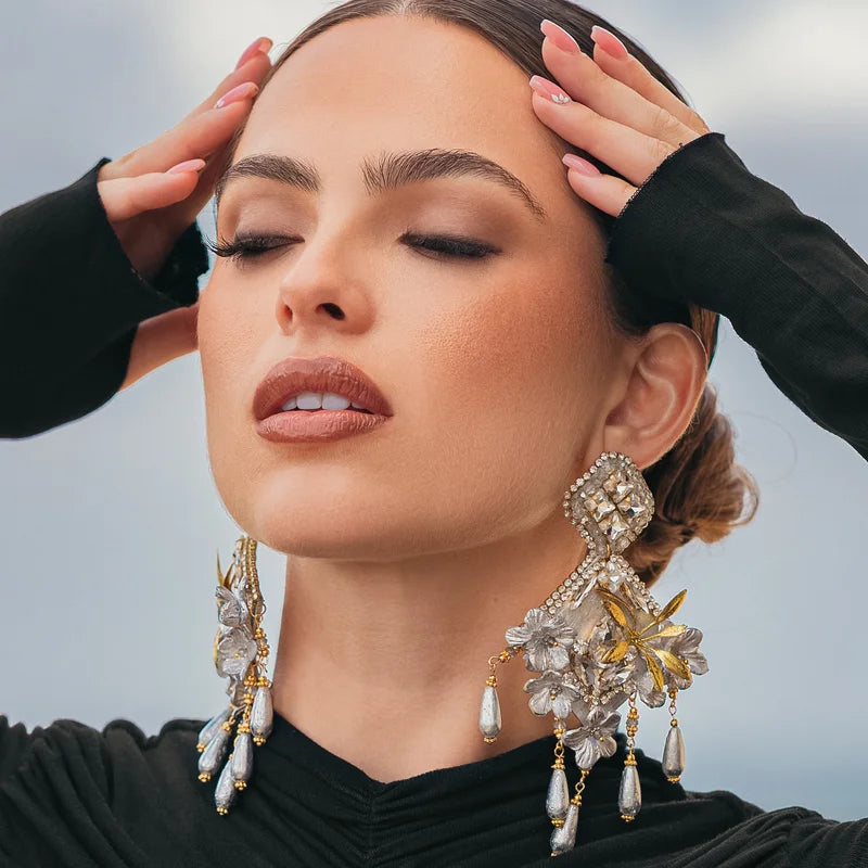 These handcrafted earrings are made from natural totumo shaped into a diamond form, featuring delicate flowers made from banana fiber and painted in silver and gold.


