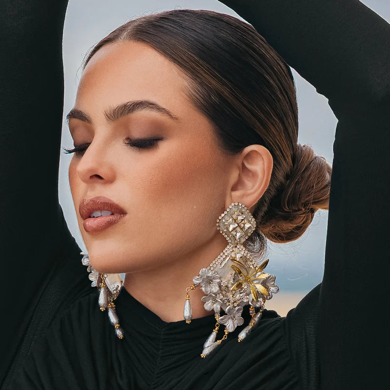 These handcrafted earrings are made from natural totumo shaped into a diamond form, featuring delicate flowers made from banana fiber and painted in silver and gold.

